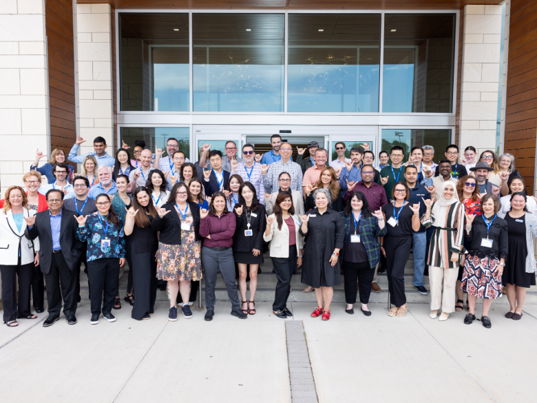 A large group of individuals stands together outside a building for a professional development event group photo.
