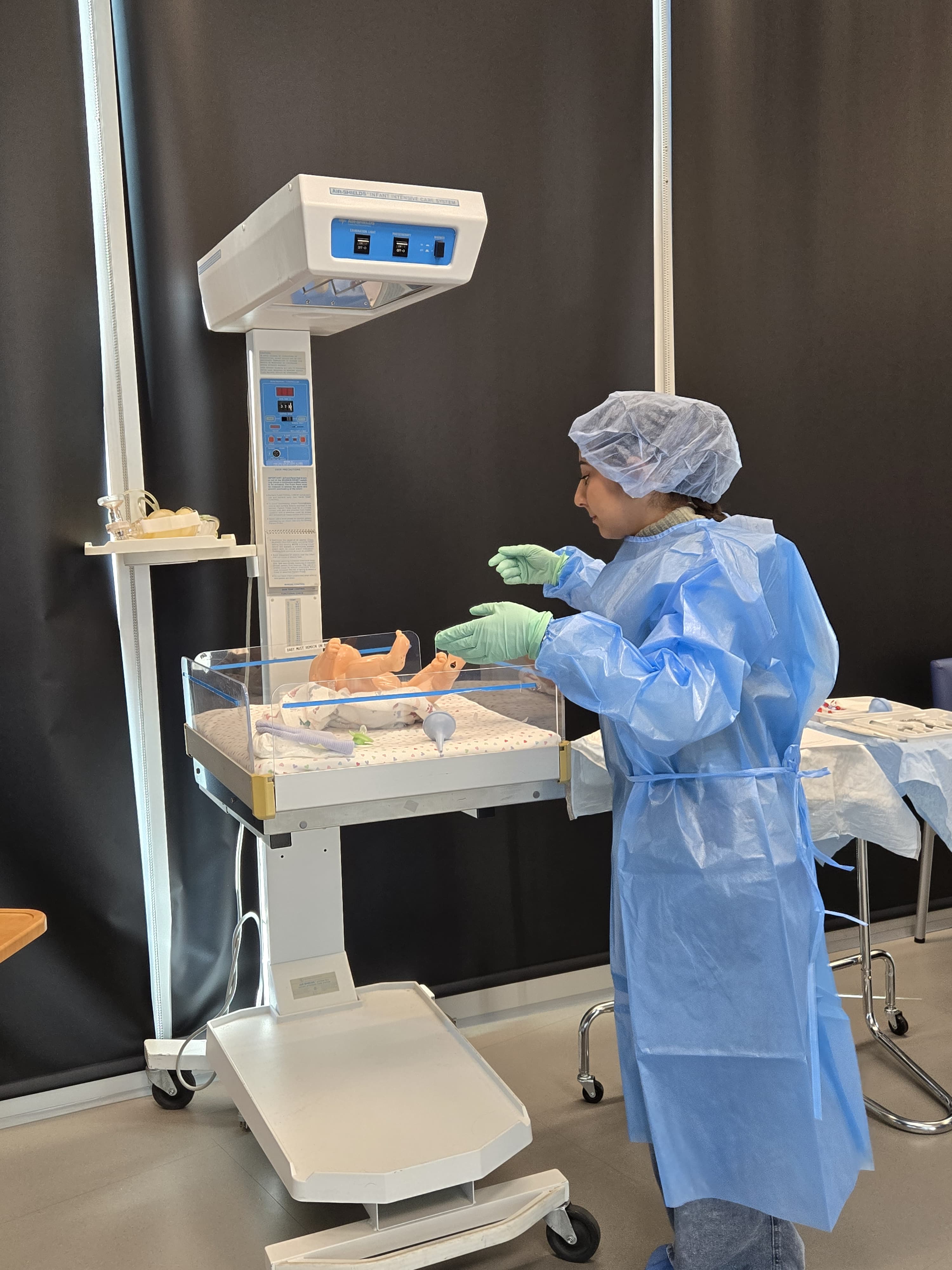 Person in blue gown interacts with infant simulation model.