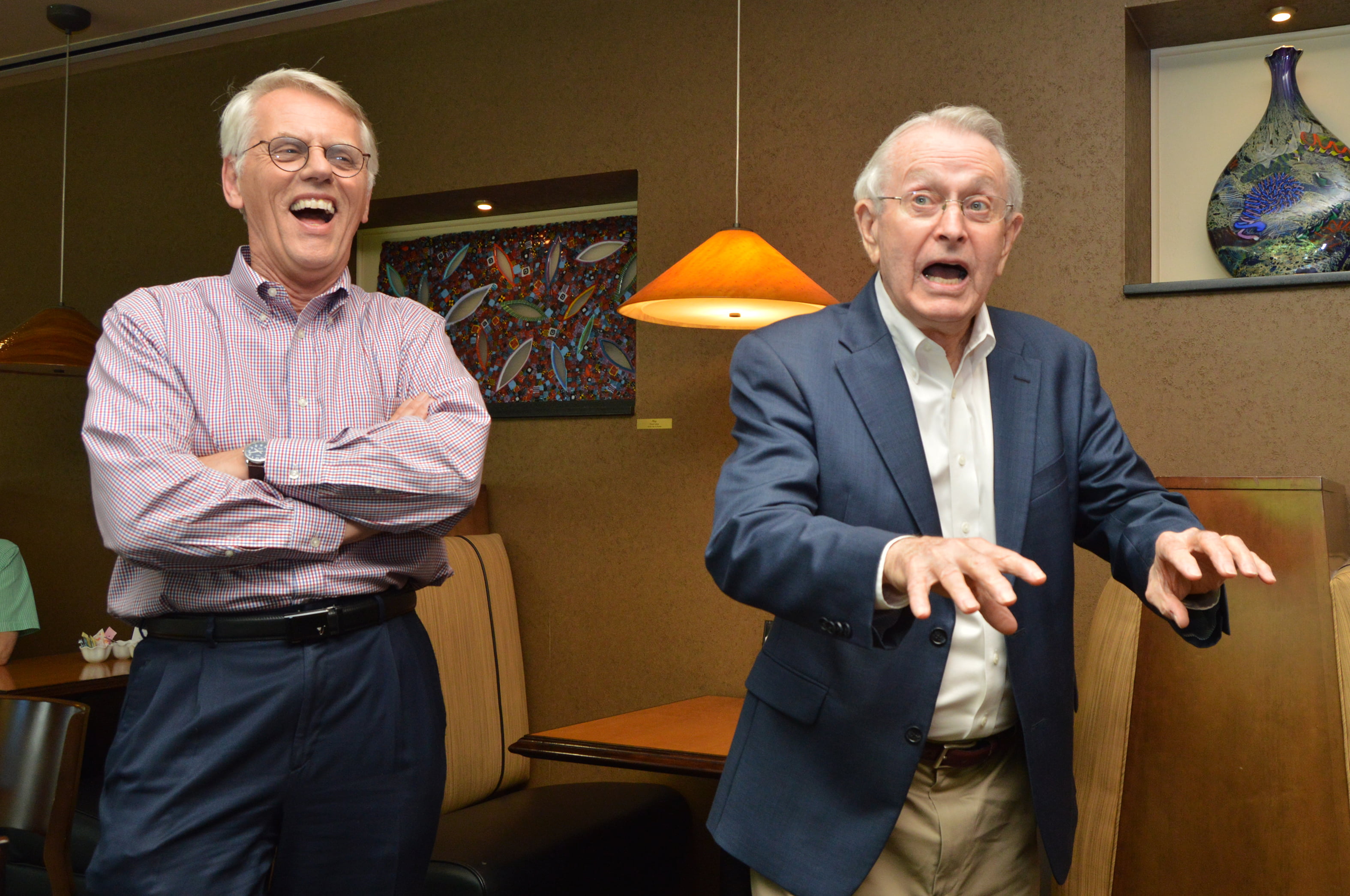 n a color photo from 2016, Verne Cox, right, wearing a blue blazer, gestures expressively with both hands and has his mouth open as if telling a story. To his left, Paul Paulus, in a checkered shirt, stands with his arms crossed, laughing heartily with his mouth wide open.