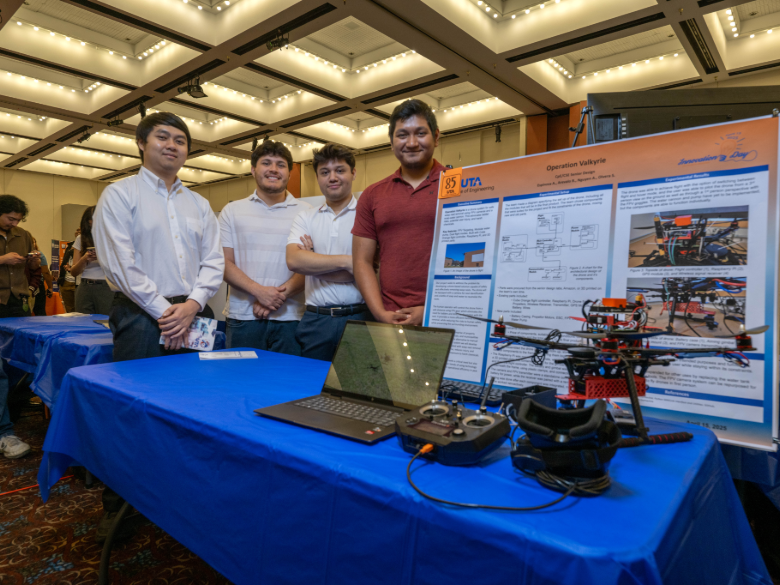 A group standing beside a project display featuring a drone, laptop, and research poster at an academic showcase event.