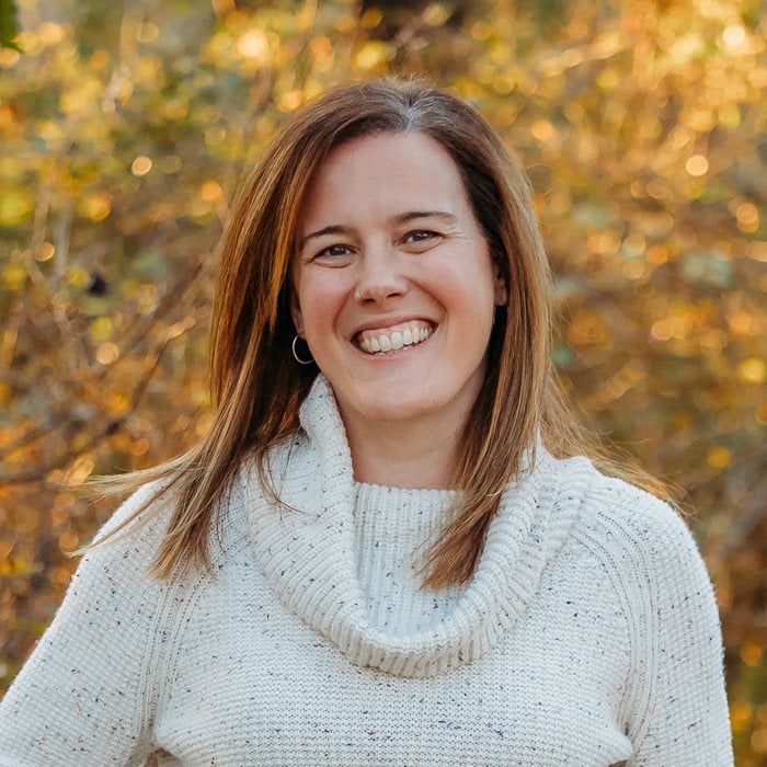 Dr. Jennifer O'Brien poses for a photo in a white sweater in front of fall foliage.