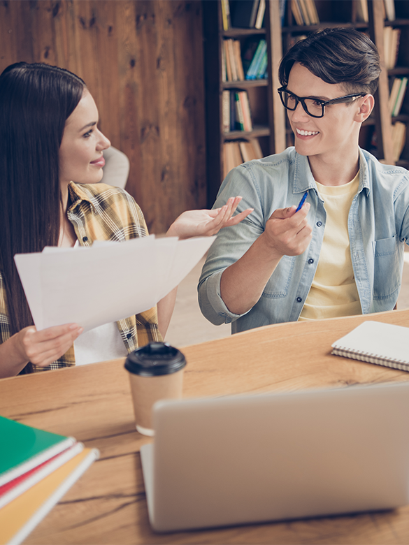 A group of students gathered around a table gently smiling to discuss writing ideas