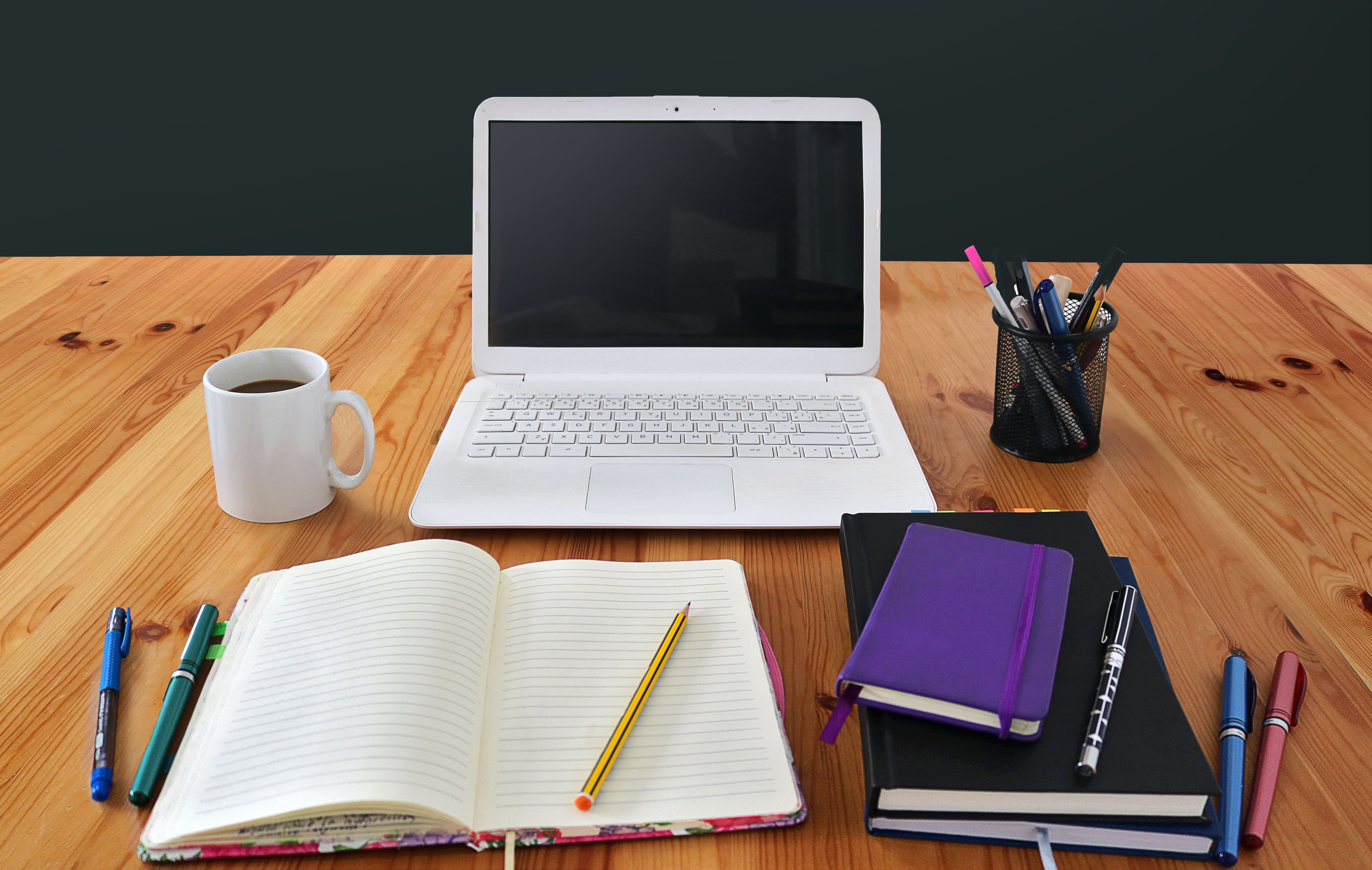 Laptop, open notebook, coffee mug, and study materials arranged on a wooden table, representing learning, teaching, and professional development in an educational setting.