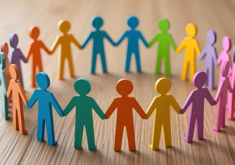 A circle of colorful paper cutout figures holding hands on a wooden surface.