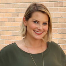 picture of Erin Carlson, dressed in a dark short-sleeve shirt with a delicate necklace in front of a brick wall