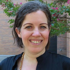 picture of Peggy Semingson, dressed in a dark shirt with a necklace in front of trees