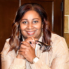 picture of Zerita Hall, dressed in blazer holding a pair of glasses with a watch and dangling earrings.