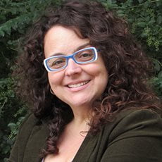 picture of Alicia Rueda-Acedo, dressed in a dark shirt with blue and white rimmed glasses