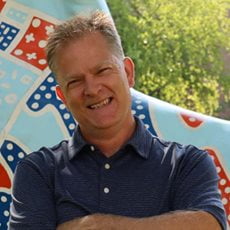 picture of Larry Nelson, dressed in a dark button up with his arms crossed in front of the U T A spirit horse by the M A C