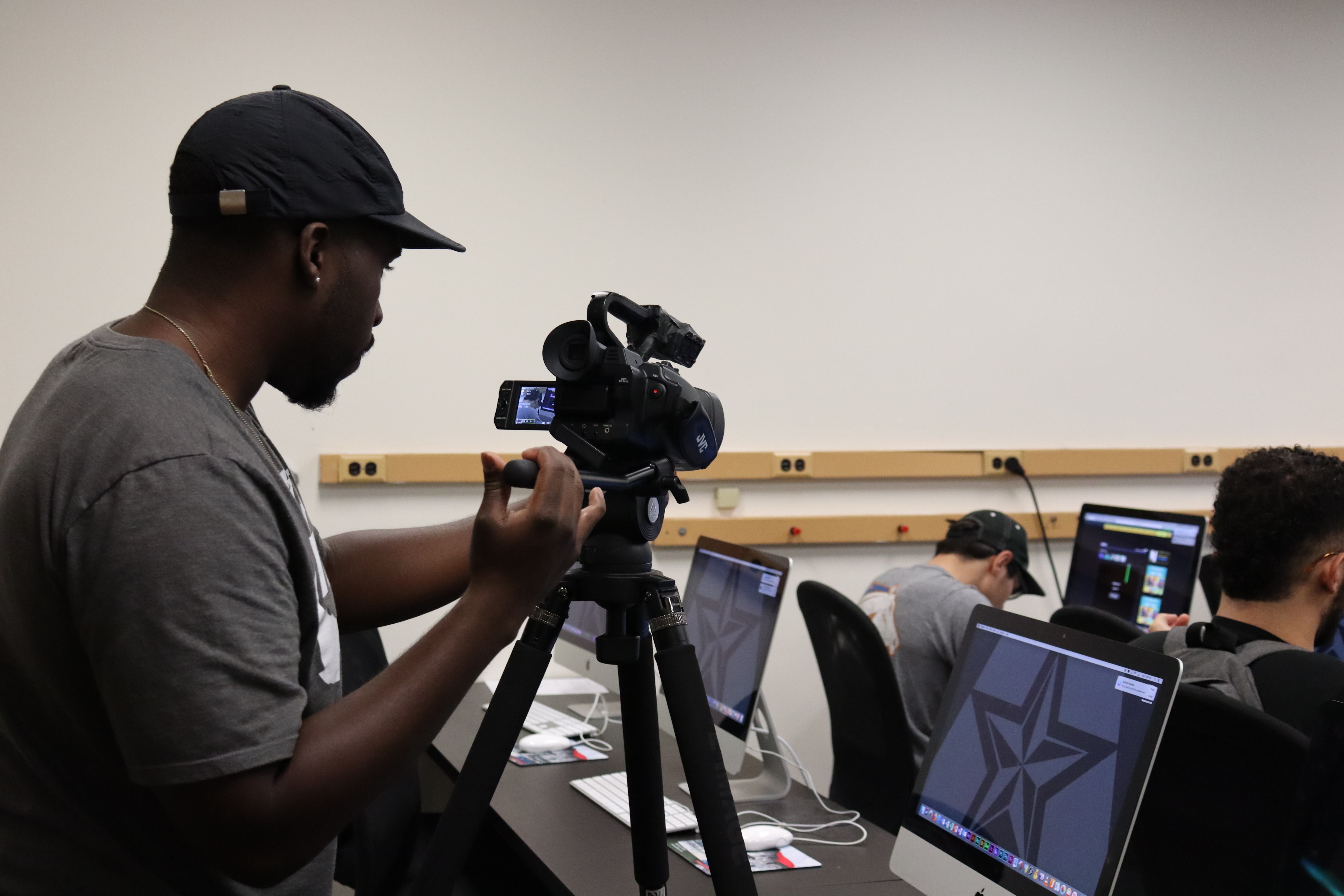 a student working on a service learning project by filming another student who's on a desktop working on an assignment