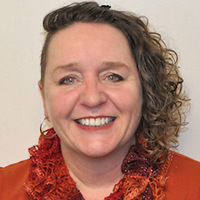 picture of Cynthia Kilpatrick, dressed in a shirt with a frilly collar with curly hair in front of a neutral background
