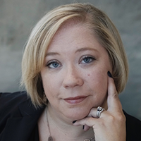 headshot of Dr. Erin Elizabeth Chernak in front of a neutral background, wearing a dark blouse, a necklace, and rings