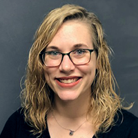 Grace Brannon dressed in a dark blouse and glasses in front of a neutral background