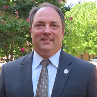 picture of Jerry Hubbard, dressed in a suit and tie in front of trees on campus