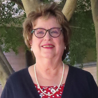 picture of Joyce Myers, dressed in a cardigan over a floral shirt with a pearl necklace, earrings, and glasses