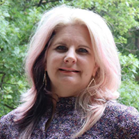 Shelley Wigley standing in front of trees with a flowery print blouse