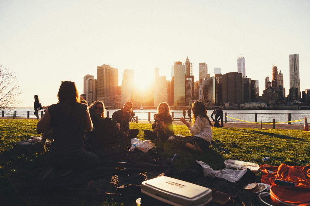 several students sitting on grass near a body of water with the sun setting in the background
