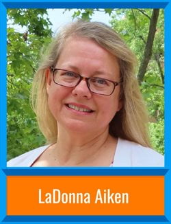 LaDonna Aiken stands in front of trees with a light cardigan and dark-rimmed glasses. There's a border around the image and her name is at the bottom, "LaDonna Aiken."