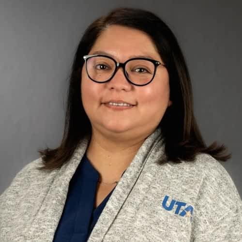 smiling woman wearing glasses and a sweater with UTA on the front