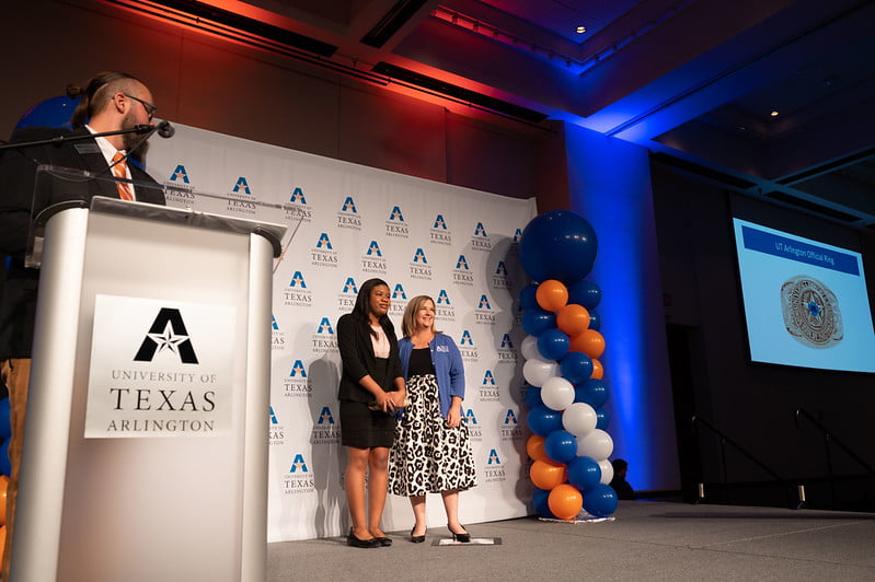 2022 Ring Ceremony stage with two people posing for photo in front of UTA banner and balloons