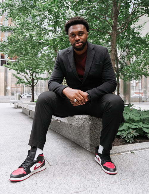 Link Kabadyundi, seated outside in black suit and gym shoes