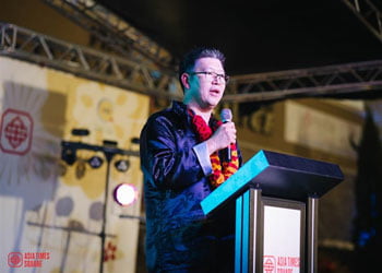 Matthew Loh speaking at a podium at an Asia Times Square event in Grand Prairie