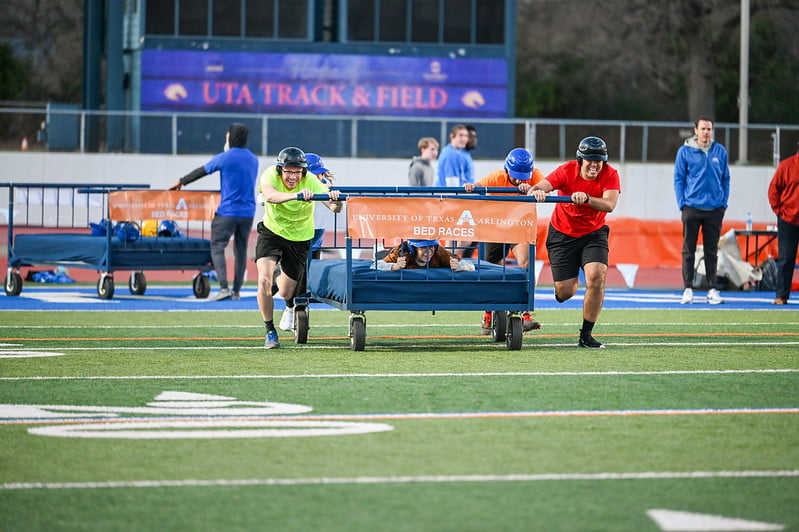 student participants running across the field with the bed in the Bed Races