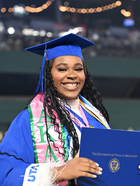 Student at graduation in regalia and holding diploma while smiling for camera