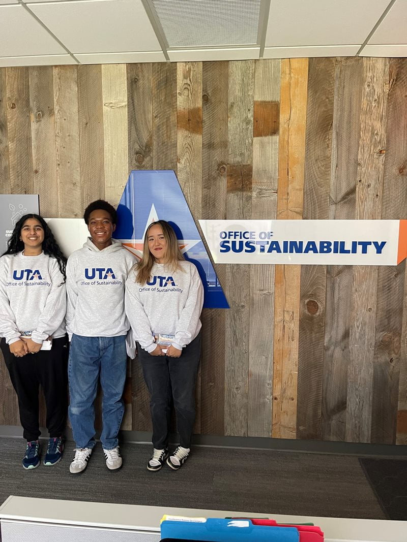 Eco-Reps smiling in front of the UTA Office of Sustainability sign.