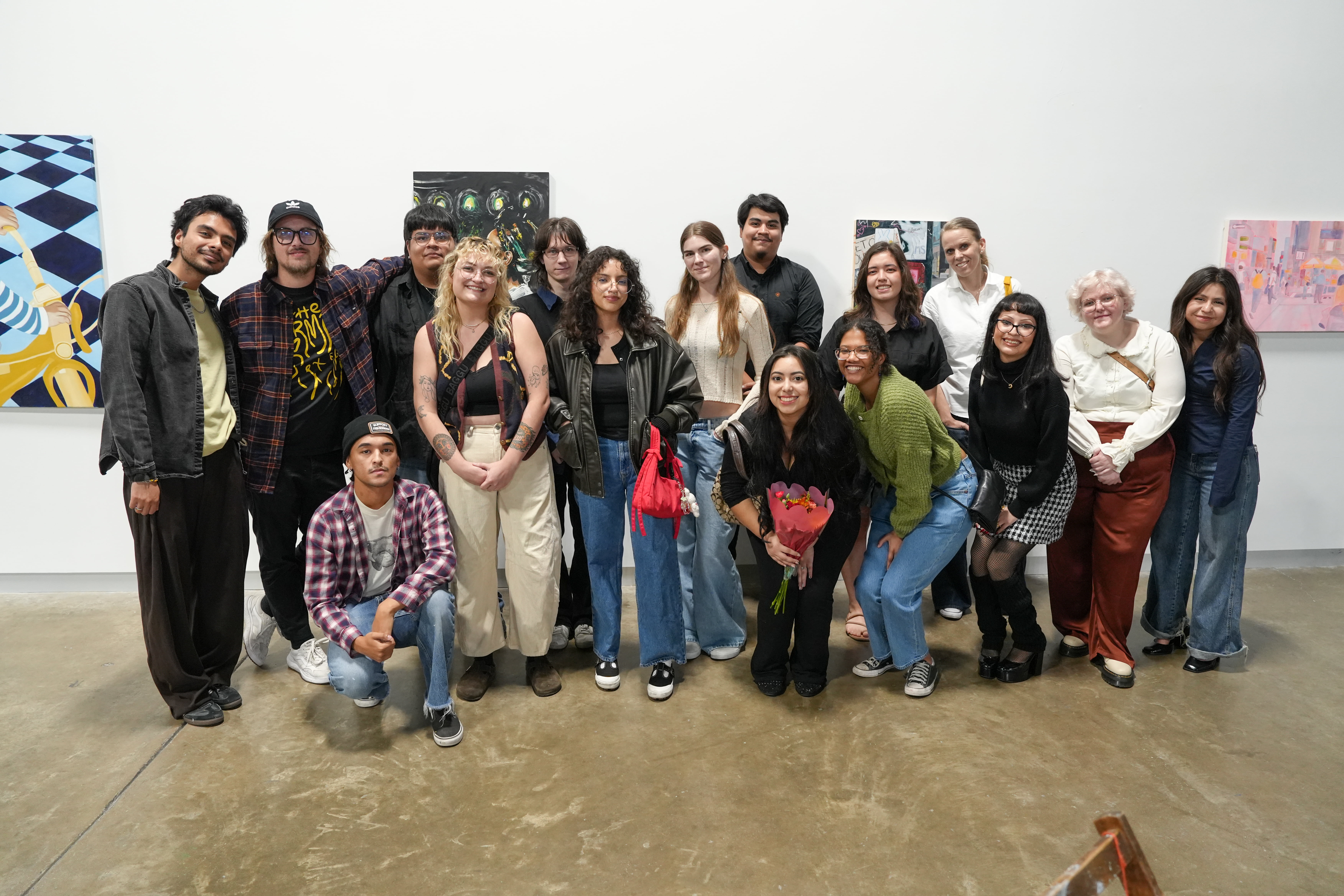 A large group of UTA art students and faculty pose together in the gallery in front of various paintings during the exhibition opening.