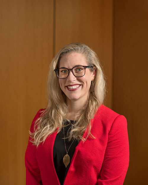 Grace Brannon in a suit, wearing glasses and a long necklace.