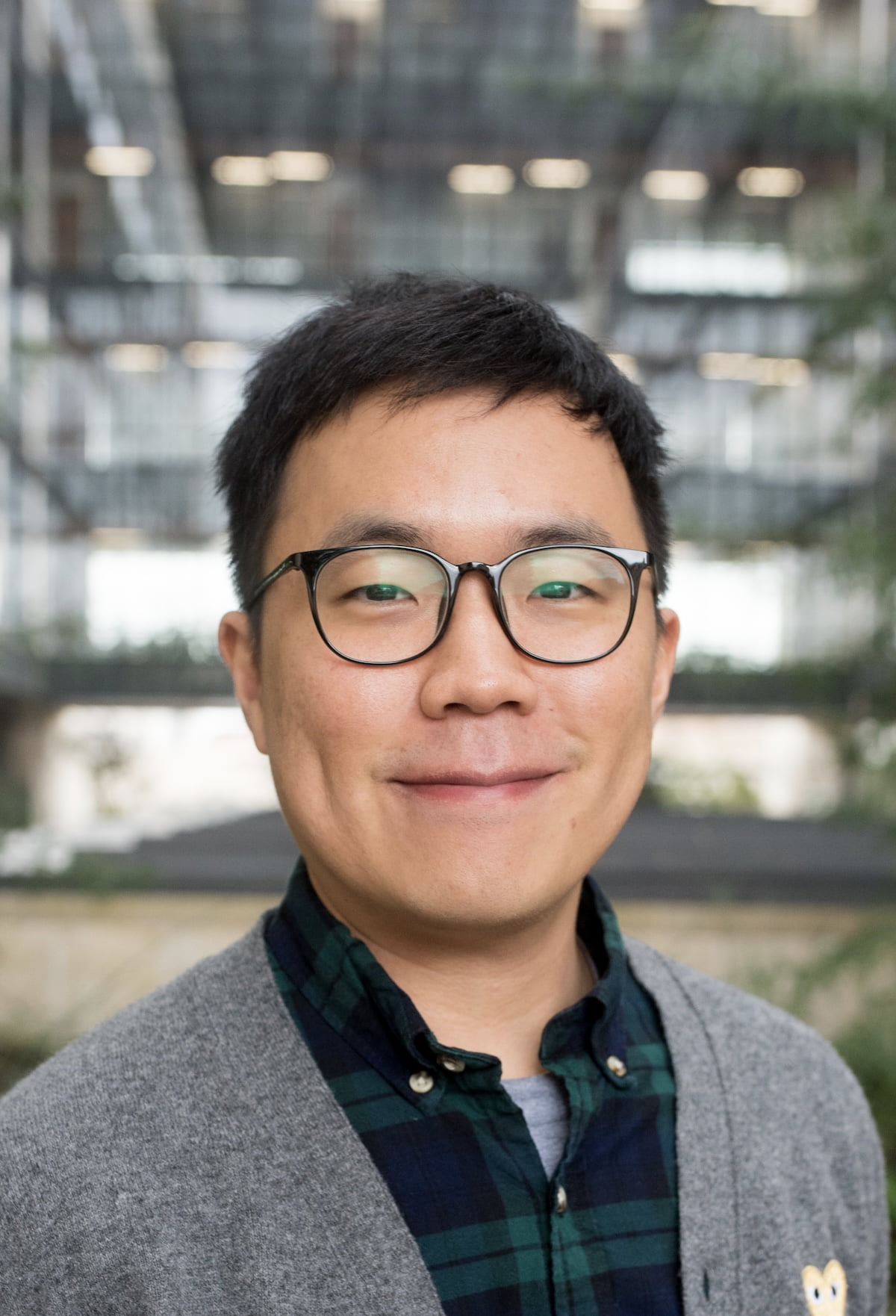 June Park smiling with short hair and glasses while wearing a button down and a sweater