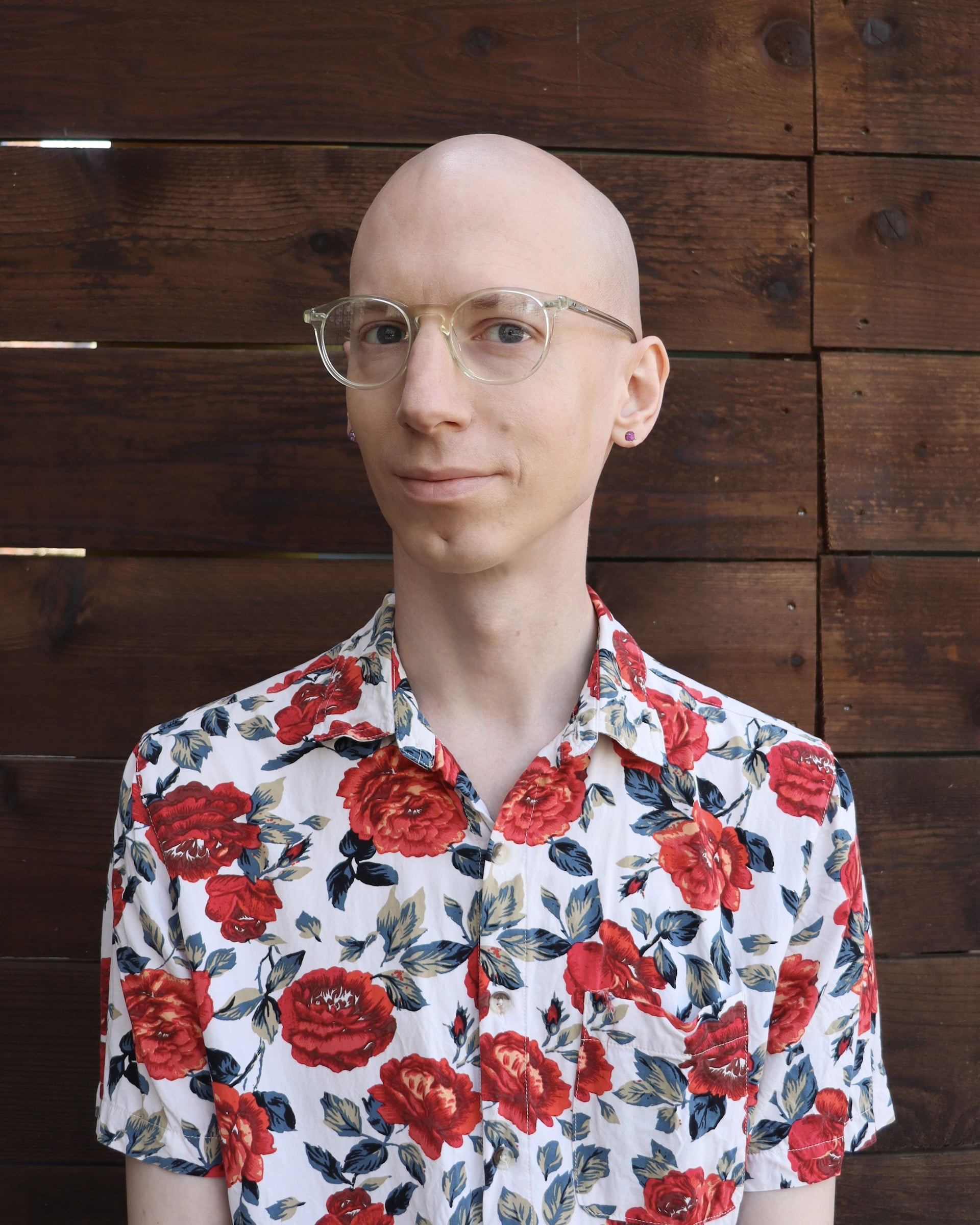 Luke Roelofs smiling with glasses, no hair, and a floral-print button up