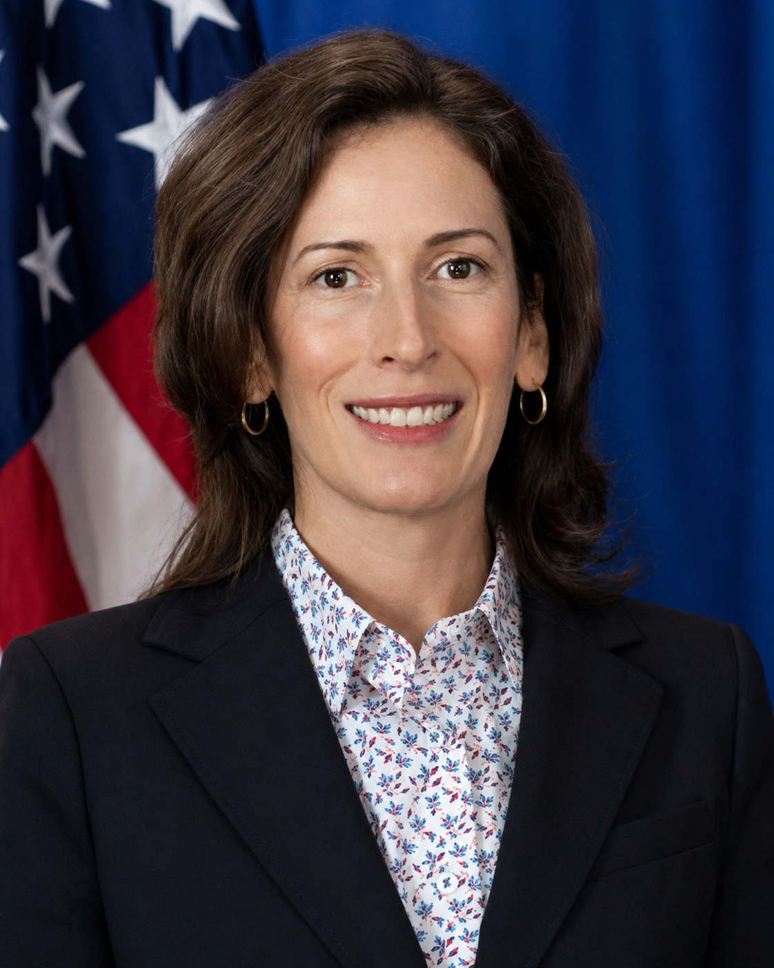 Christine Meyer in a suit, standing in front of the American flag.