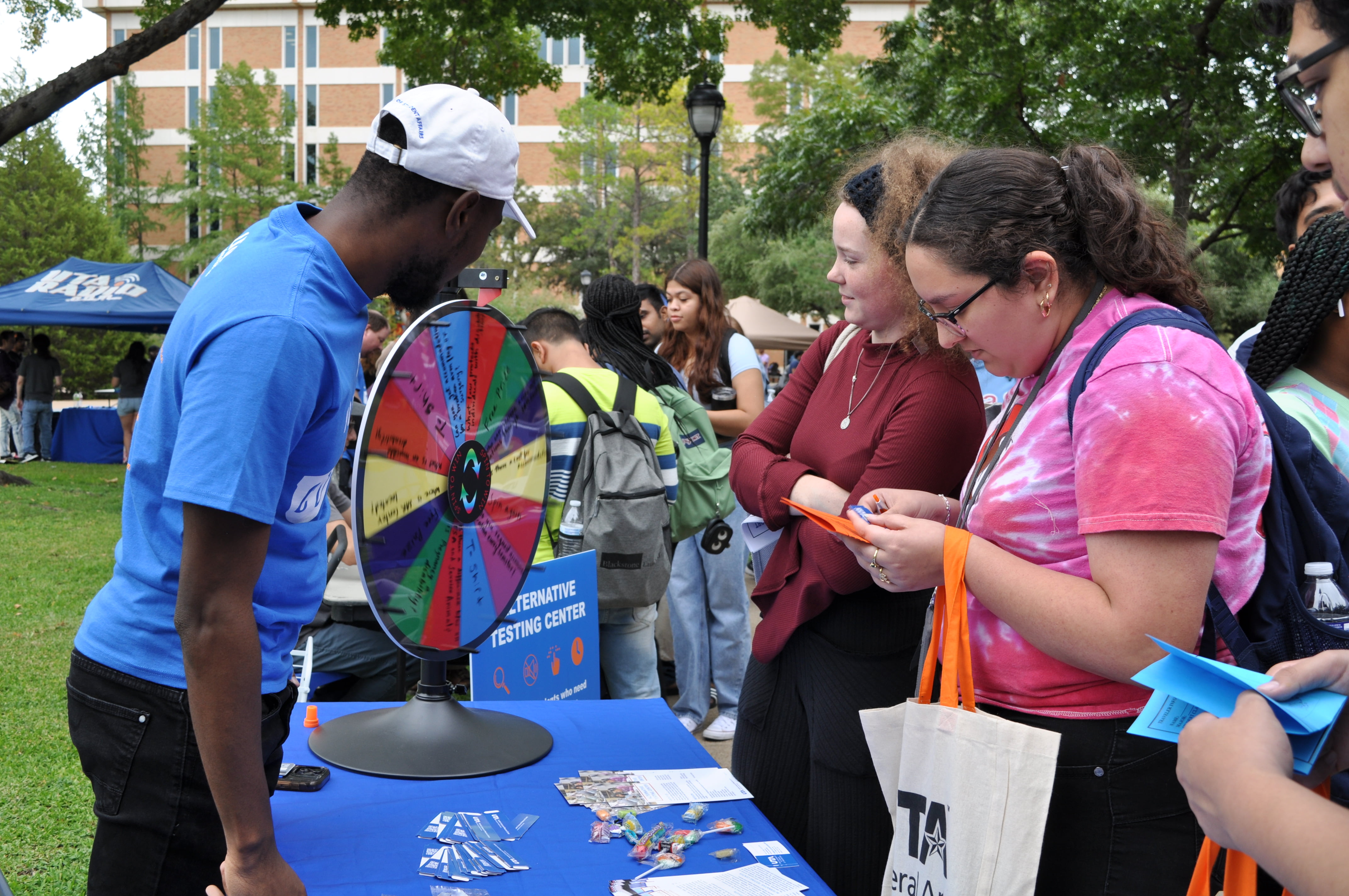Students around a COLA info table, playing a spin-to-win wheel game.