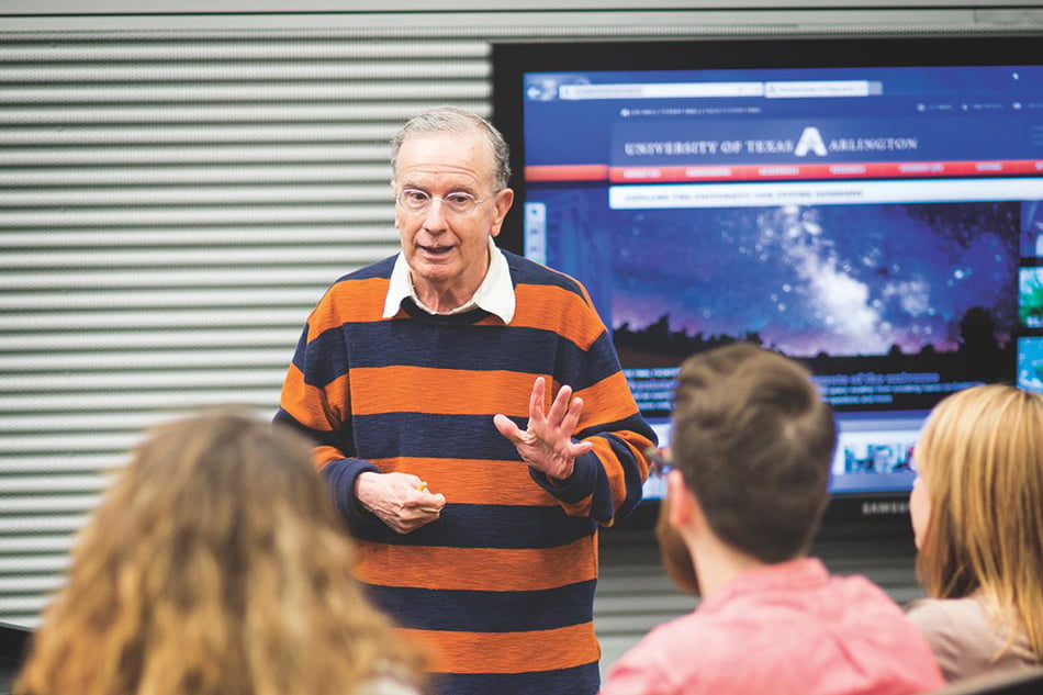Dr. Allan Saxe in front of a group of students, wearing a horizontal striped polo shirt.