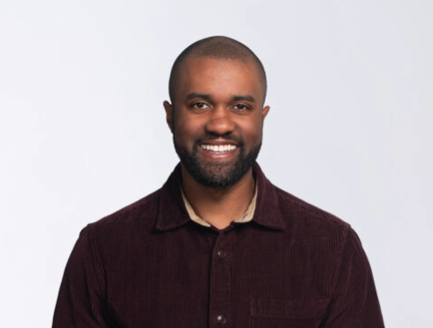 Gerrell Williams smiling at the camera wearing a dark button up in front of a plain backdrop
