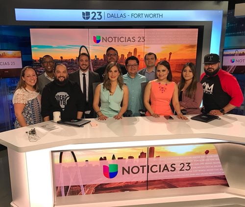 Omar and coworkers behind the news desk, smiling.