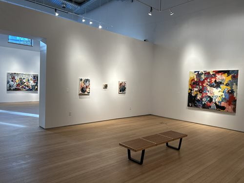 A gallery with multiple paintings hanging up on the walls
