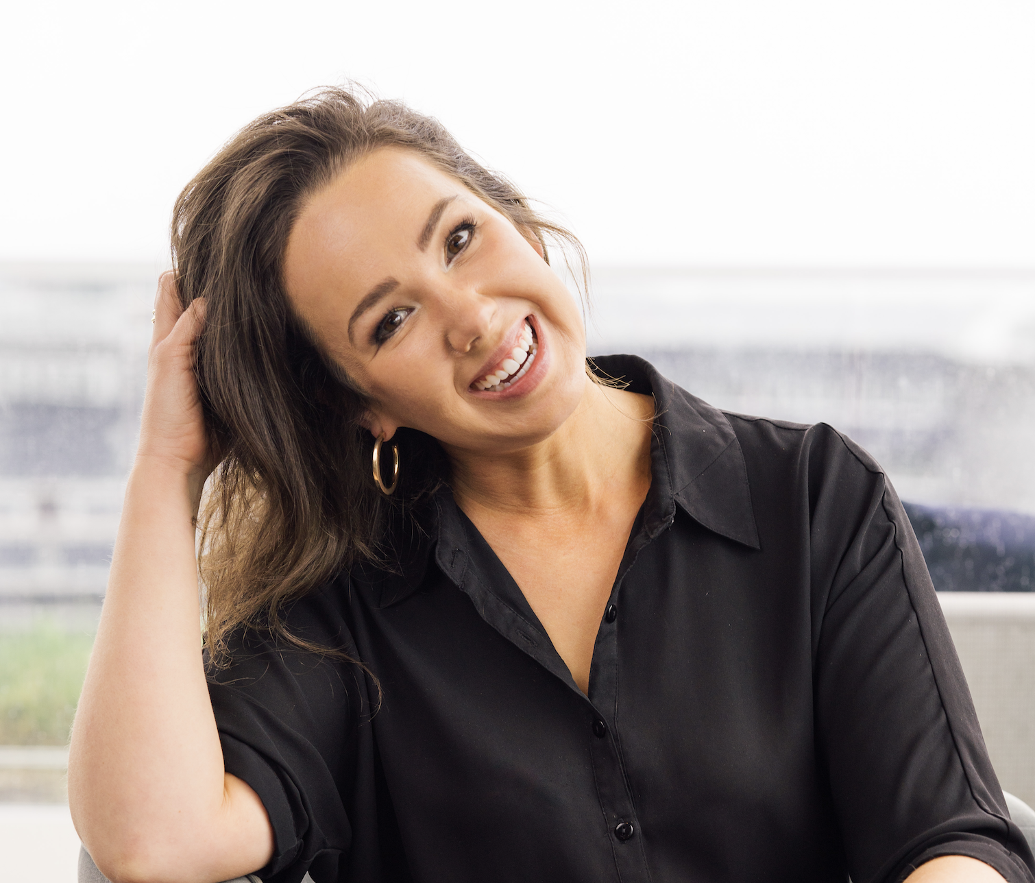 Lauren Devoll sitting in a chair, leaning on the arm rest and wearing a button up and slacks.