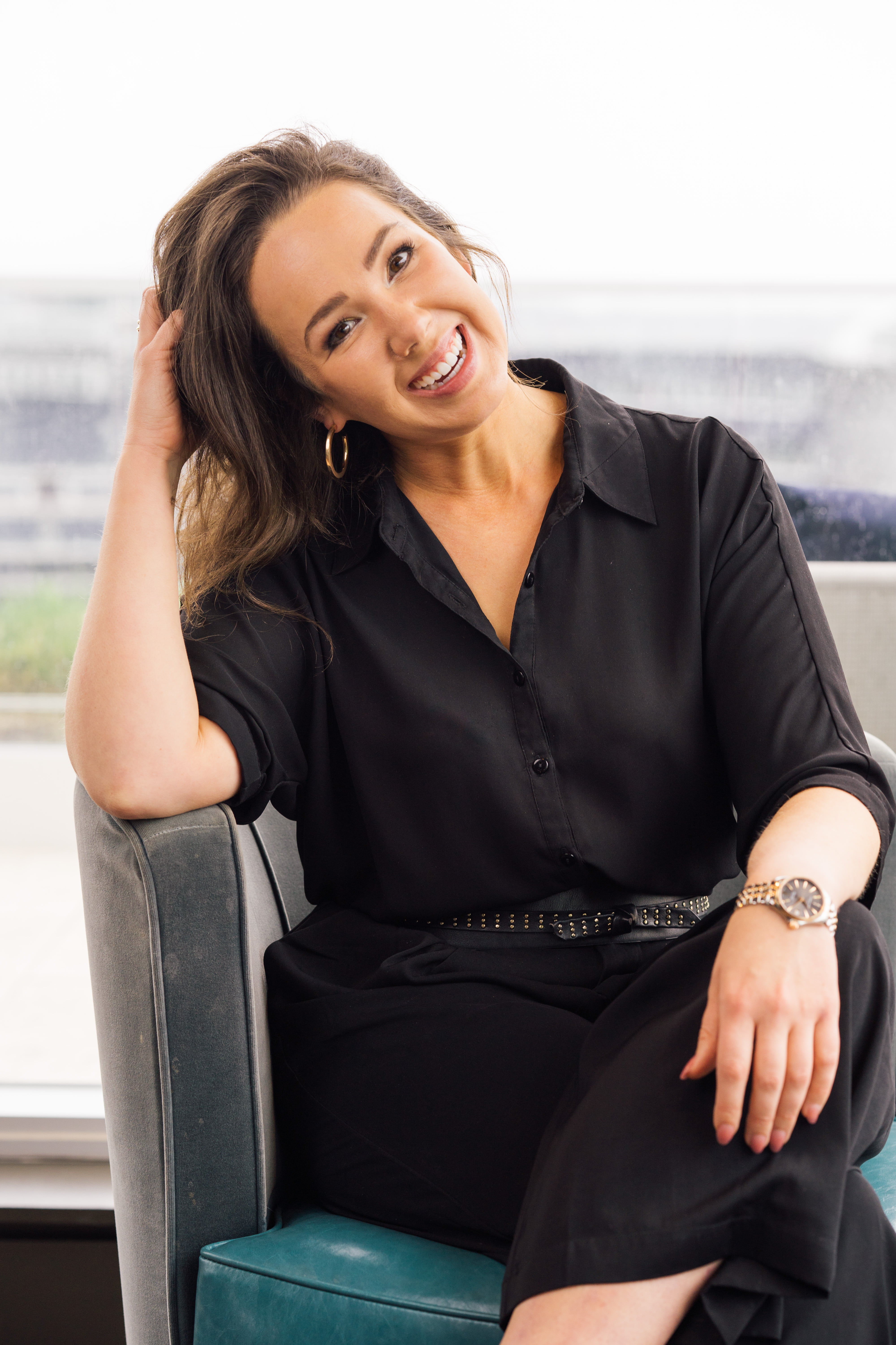 Lauren Devoll sitting in a chair, leaning on the arm rest and wearing a button up and slacks.