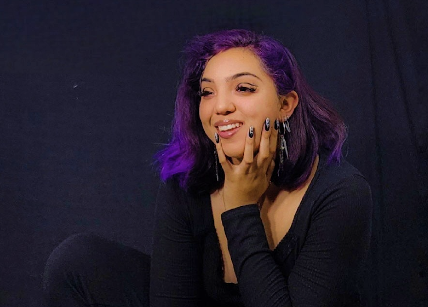 Luz Lopez looking off to the side, smiling and dressed in all dark clothes