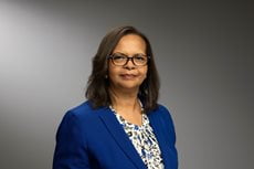 Angela Avery wearing a blazer on top of a patterned blouse and glasses.