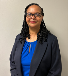 Angela Avery wearing a blazer on top of a solid colored blouse, wearing glasses and matching perl earrings and necklace.