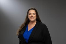 Dean Elizabeth Newman smiling with medium hair, a blazer, and a U T A colored button up.