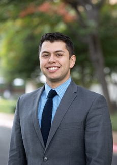 Justin Silcox wearing a suit and smiling with trees in the background