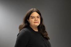 Maria Carmona headshot, wearing a long sleeve shirt, glasses, and a necklace with medium-length hair.