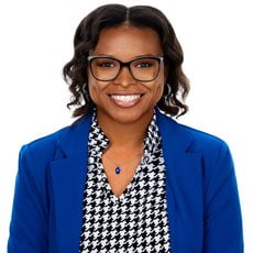 Reyunia Holmes smiling with glasses, a patterned button up, and blazer.