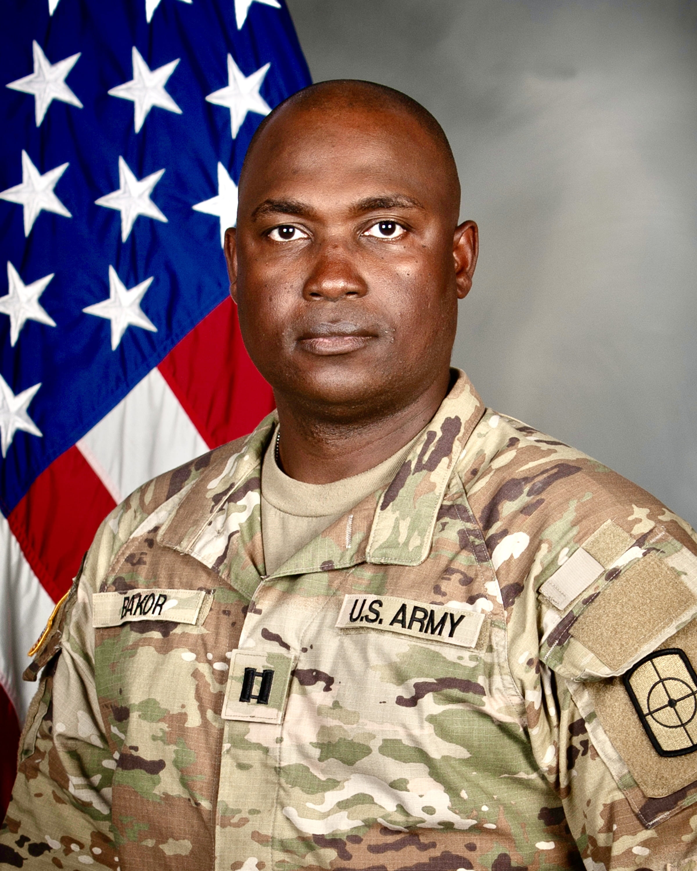 CPT Barinedum Bakor standing in front of the American flag.
