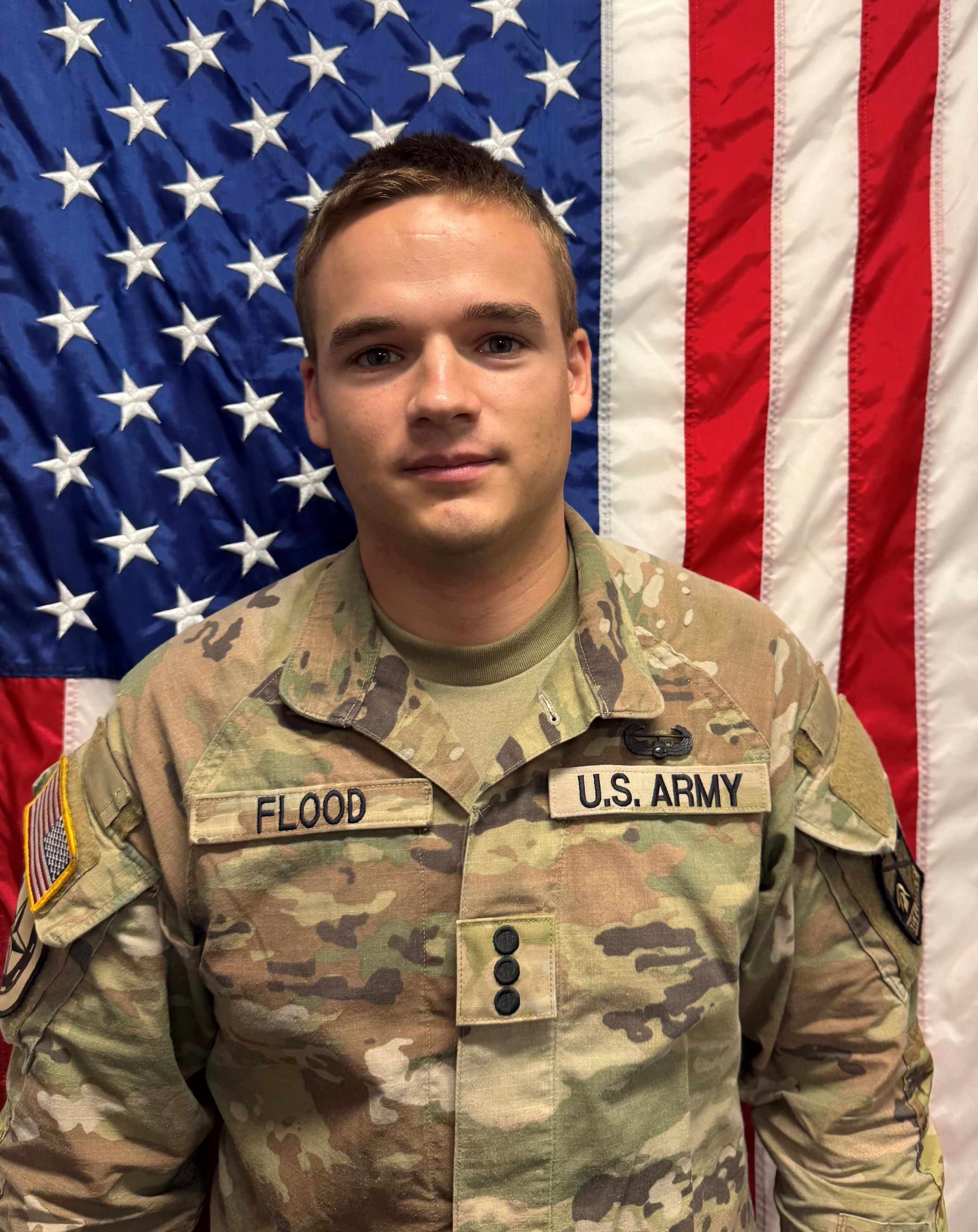 Cadet Flood standing in front of a U S A flag in uniform.